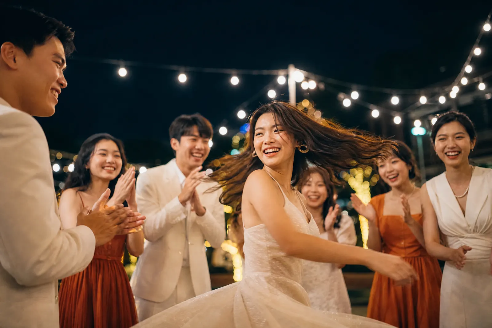 Nhóm sinh viên nhảy và cười dưới ánh đèn dây trong buổi chụp kỷ yếu ban đêm