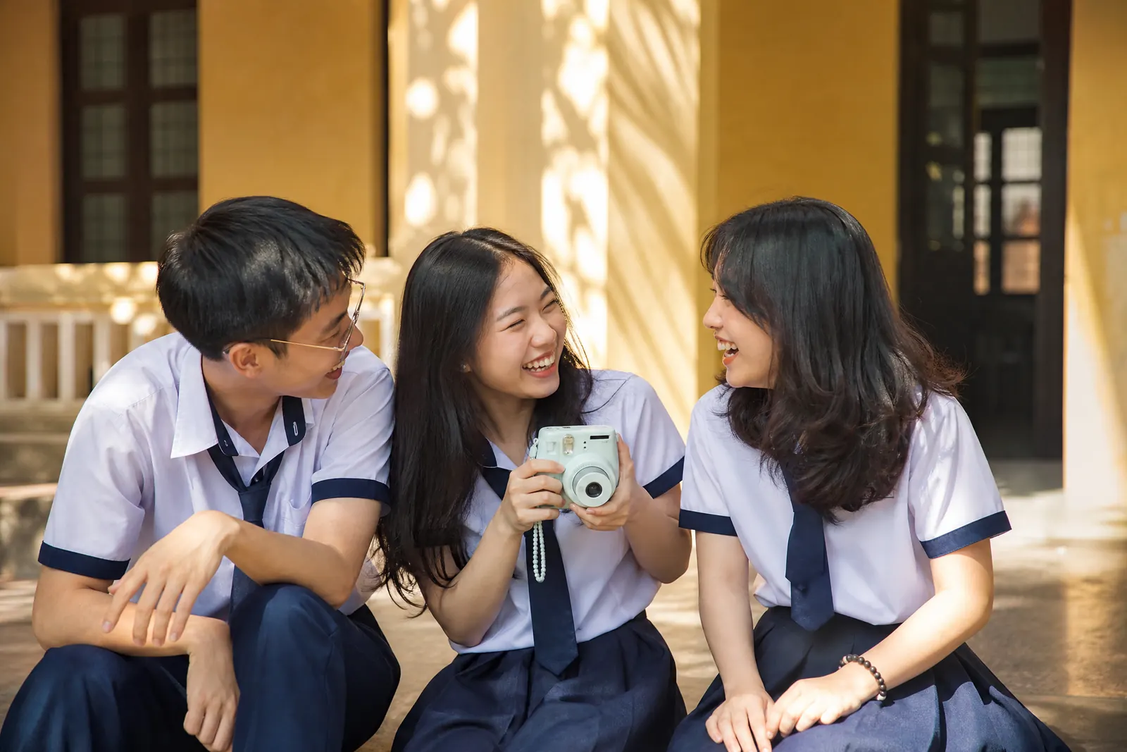 Ba học sinh cười tự nhiên trên bậc thềm trường trong buổi chụp kỷ yếu